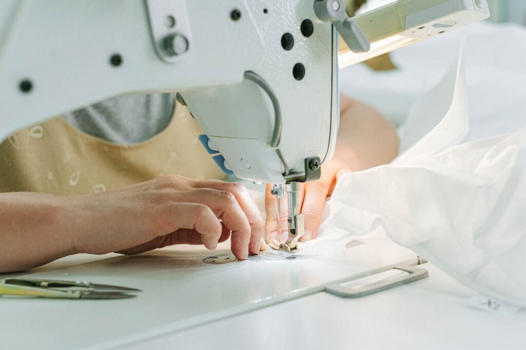 A seamstress using a sewing machine in a workshop, highlighting hands and fabric.